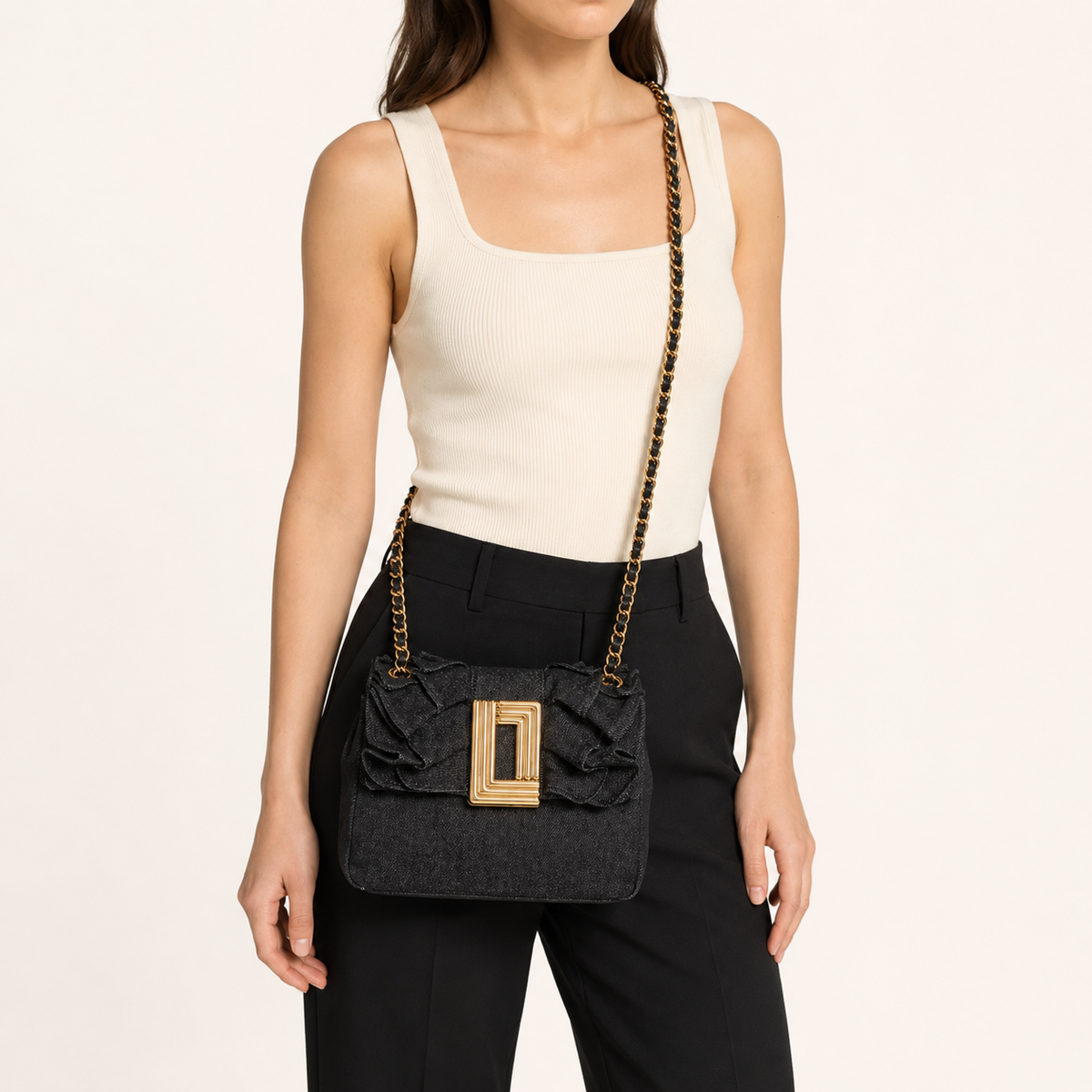 Woman wearing a black textured crossbody bag with a gold chain strap and gold buckle.